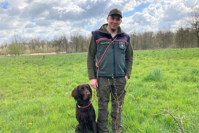 Bezirksförster Tizian Bootz aus Recklinghausen steht mit seinem Hund auf einer Wiese.