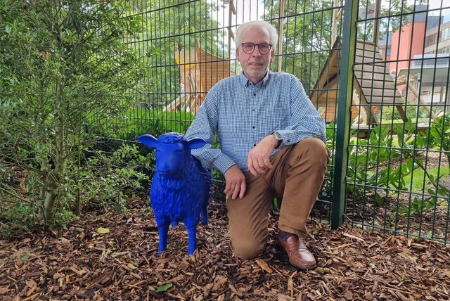 Ein Mann kniet neben einem blauen Schaf