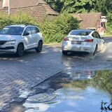 Zwei Autos fahren auf einer Straße an großen Pfützen vorbei.