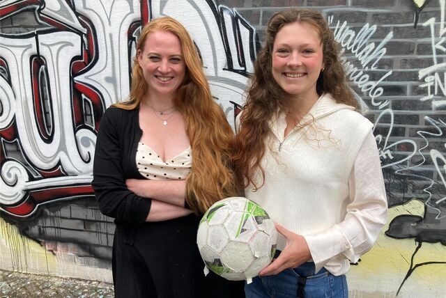 Birte Gooßes (l.) und Emely Lukasiewiecz stehen mit einem Fußball in der Hand auf dem Hof der Altstadtschmiede vor einer Graffiti-Wand,