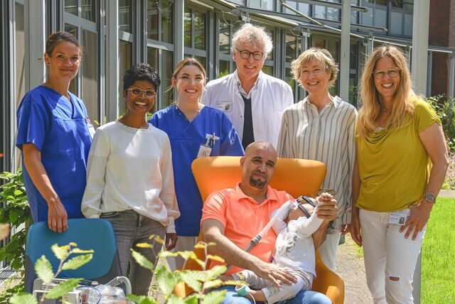 Eine Gruppe Menschen steht hinter einem Mann, der sitzt und ein Kind auf dem Schoß hat