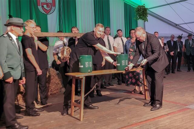 Ein Mann schlägt vor einer Gruppe Schützen ein Bierfass an.
