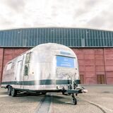Ein metallener Trailer-Anhänger steht vor einer Industriehalle.
