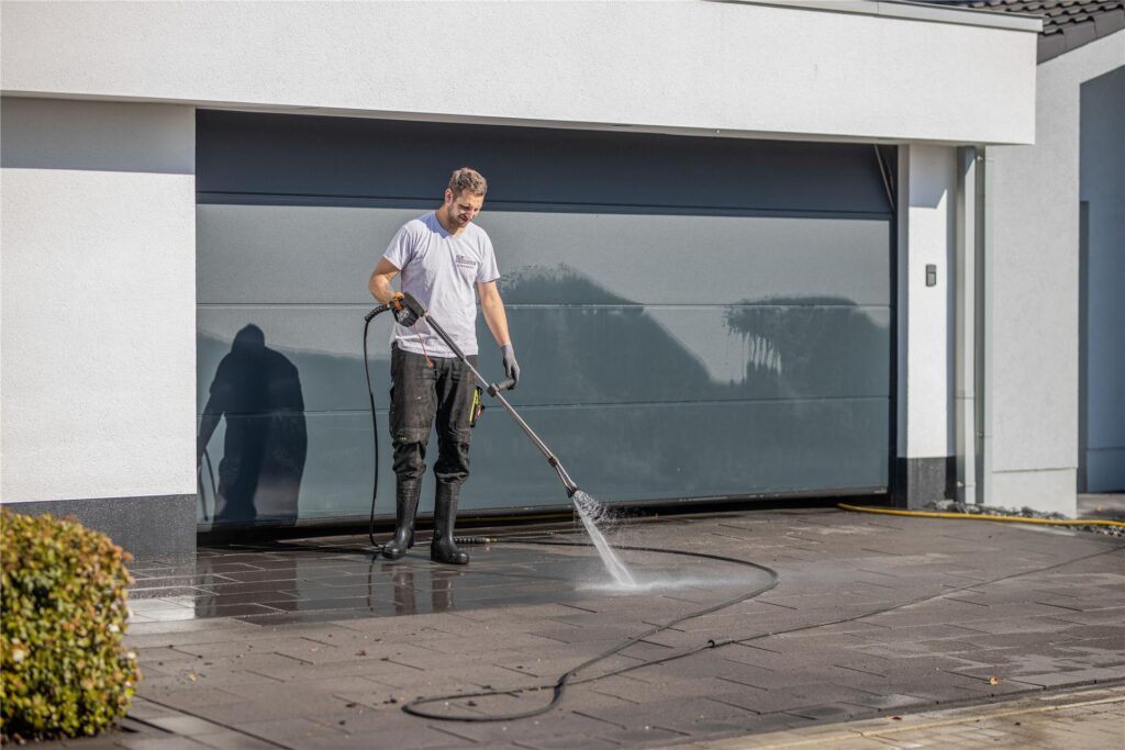 Ein Mann reinigt eine gepflasterte Garagenauffahrt. Ein Mann reinigt eine gepflasterte Garagenauffahrt.