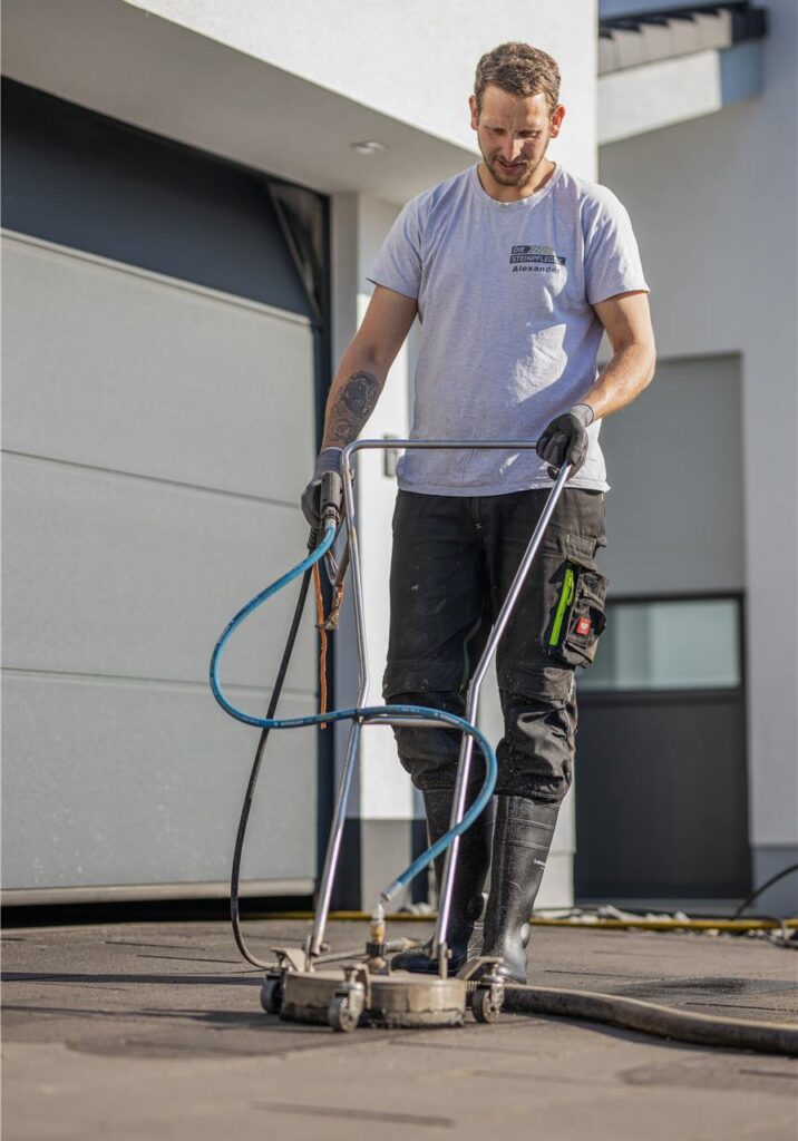 Ein Mann reinigt das Pflaster einer Auffahrt mit einer Profi-Maschine Ein Mann reinigt das Pflaster einer Auffahrt mit einer Profi-Maschine