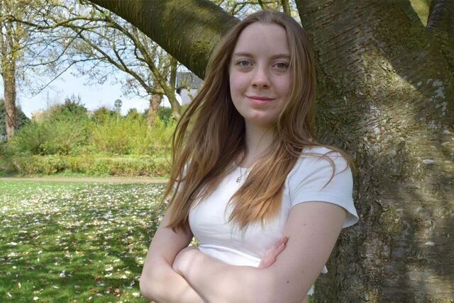 Luise Storm lehnt sich an einem Baum an. Im Hintergrund sind Grünflächen zu sehen.
