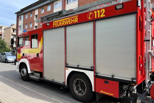 Ein Feuerhwehrwagen der Stadt Herten steht format-füllend im Bild. Die Front ist in Richtung des linken Bildrandes ausgerichtet. Im Hintergrund ist ein kleines Stück blauer Himmel, sowie einige Mehrfamilienhäuser zu erkennen.