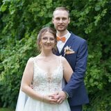 Rebecca und Gerrit stehen zusammen. Im Hintergrund sind grüne Bäume zu sehen.