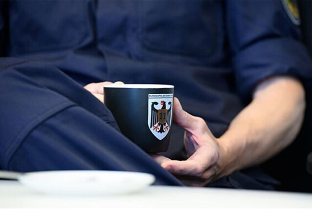 Polizist in blauer Uniform sitzt mit Kaffeetasse am Tisch