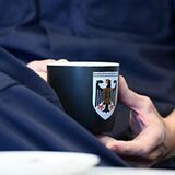 Polizist in blauer Uniform sitzt mit Kaffeetasse am Tisch