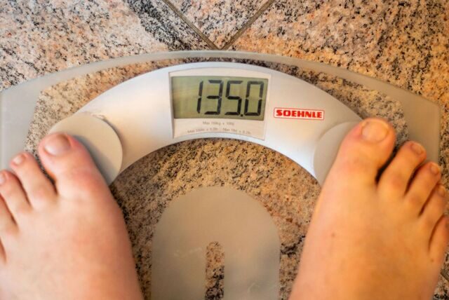 Füße auf einer Waage, die ein Gewicht von 135 Kilo anzeigt.