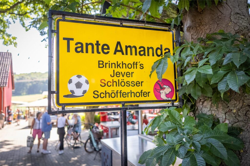 Schwarze Schrift auf gelbem Untergrund: Das Schild von Tante Amanda ist einem Ortseingangsschild nachempfunden. Darunter aufgezählt sind die Biersorten, die man hier vom Fass bekommen kann.