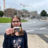 Katharina Göke steht mit dem DeutschlandTicket in der Hand vorm Kreisverkehr. Im Hintergrund ist der Busbahnhof Herten-Mitte zu erahnen.