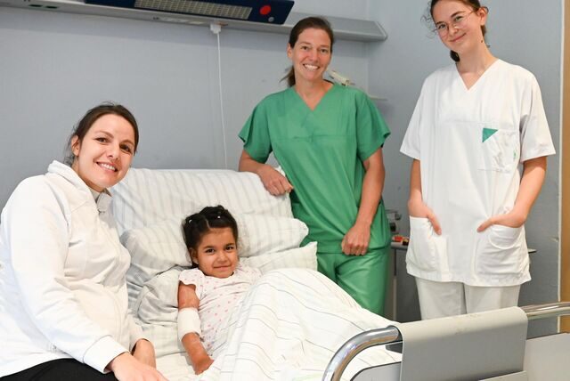 Die fünfjährige Fatma aus Afghanistan liegt mit ihren erfolgreich behandelten Wunden im Krankenbett. Umgeben ist sie von drei Beschäftigten des Klinikums in Dortmund.