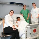 Die fünfjährige Fatma aus Afghanistan liegt mit ihren erfolgreich behandelten Wunden im Krankenbett. Umgeben ist sie von drei Beschäftigten des Klinikums in Dortmund.