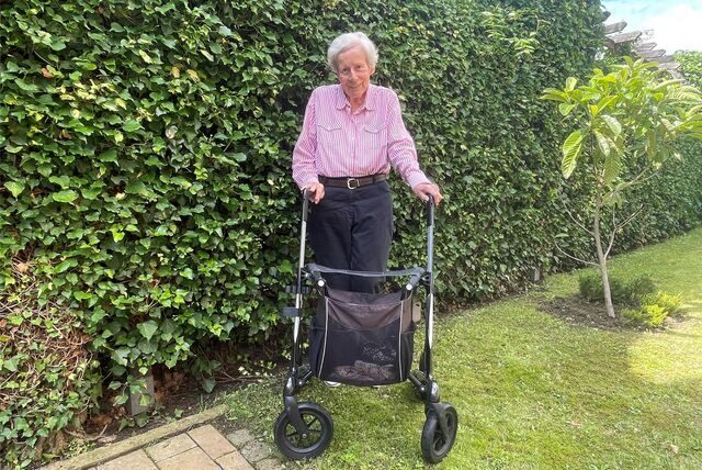 Dorothee Molitor aus Recklinghausen steht mit ihrem Rollator in Garten vor einer hohen Hecke.