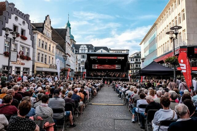 Auf dem Altstadtmarkt in Recklinghausen steht eine große Bühne, darauf spielt die Neue Philharmonie Westfalen. Auf Stühlen vor der Bühne sitzen Hunderte Zuhörer.