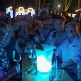 Eine Gruppe Menschen sitzt an einem Tisch. Vor ihnen steht ein beleuchteter Weinkühler.