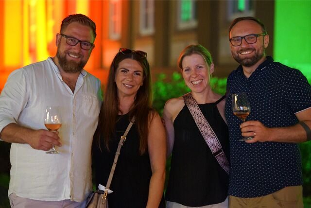 Zwei Männer und zwei Frauen. Die Männer halten jeweils ein Glas Wein in der Hand.