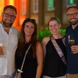 Zwei Männer und zwei Frauen. Die Männer halten jeweils ein Glas Wein in der Hand.