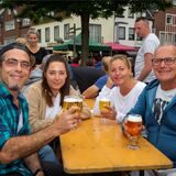 Vier Menschen sitzen an einem Biertisch und prosten in die Kamera.