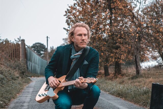Der Sänger und Gitarrist Phil Solo hockt mit einer E-Gitarre auf einem Weg.