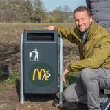 Markus von Gilardi hockt neben einem Mülleimer, auf dem ein McDonalds-Aufkleber zu sehen ist.
