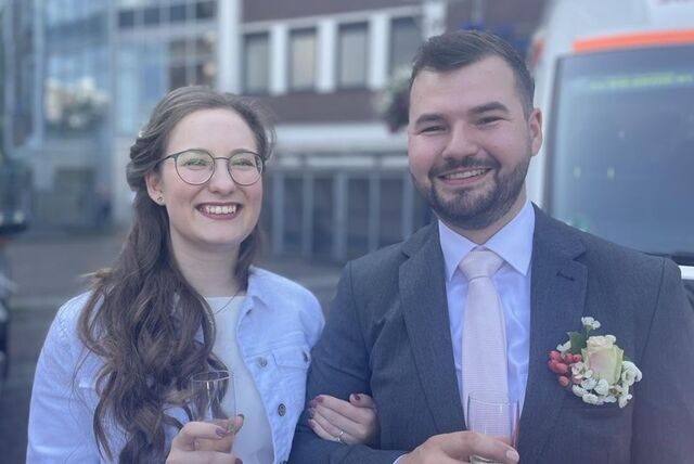 Paula und Fabian stehen nach ihrer Trauung auf dem Friedensplatz in Dortmund. Im Hintergrund ist ein Rettungswagen zu sehen.