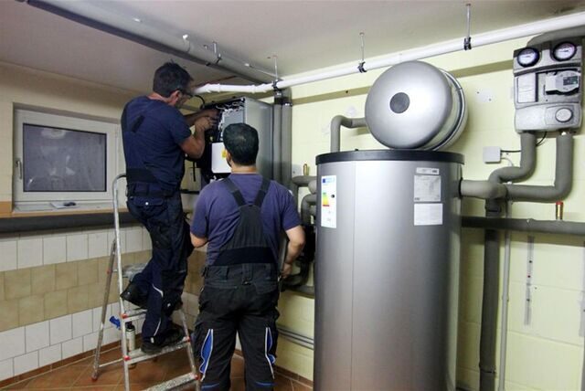 Zwei Handwerker stellen eine gerade installierte Wärmepumpe im Keller einer Doppelhaushälfte ein.