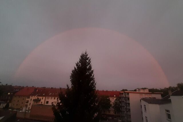 Ein rötlicher Bogen ist am Himmel zu sehen. Im Vordergrund eine Wohnsiedlung.