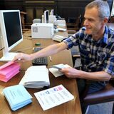 Ein Mitarbeiter der Stadt Datteln sitzt an einem Tisch, vor sich einen Monitor, eine Tastatur und verschiedene Papier-Stapel mit Unterlagen für eine Wahl. (Archivbild)