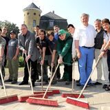Mehrere Erwachsene und Jugendliche tun fürs Foto so, als würden sie mit roten Besen eine Pflasterfläche fegen. Im Hintergrund ist das Schloss Horneburg zu sehen.