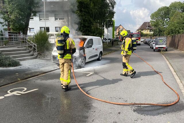 Feuerwehrleute löschen ein brennendes Auto.