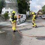 Feuerwehrleute löschen ein brennendes Auto.