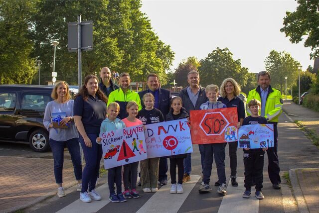 Bürgermeister, Polizei, Ordnungsamt und Kinder stehen auf dem Zebrastreifen und halten Plakate hoch.