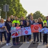 Bürgermeister, Polizei, Ordnungsamt und Kinder stehen auf dem Zebrastreifen und halten Plakate hoch.
