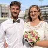 Das Ehepaar Schaefer steht nach seiner Trauung auf dem Friedensplatz vor dem Dortmunder Standesamt. Die Sonne scheint ihnen ins Gesicht.