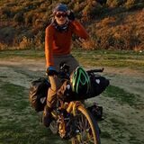 Pia auf einem Fahrrad mitten in einer grünen Landschaft. Durch eine Sonnenbrille schaut sie in die Kamera.