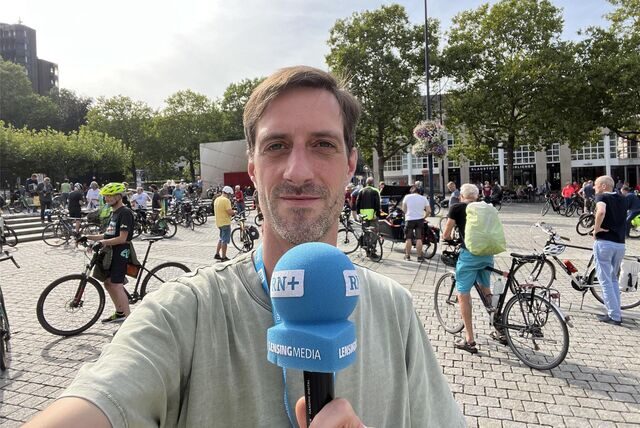 Ein Mann mit einem Mikrofon steht vor mehreren Fahrradfahrern