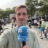 Ein Mann mit einem Mikrofon steht vor mehreren Fahrradfahrern