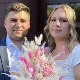 Das Ehepaar Bermel steht nach der Trauung vor dem Dortmunder Standesamt. Die Braut hält einen Blumenstrauß mit pinken Blüten und Pampasgras in der Hand.