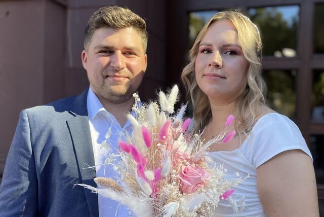 Das Ehepaar Bermel steht nach der Trauung vor dem Dortmunder Standesamt. Die Braut hält einen Blumenstrauß mit pinken Blüten und Pampasgras in der Hand.