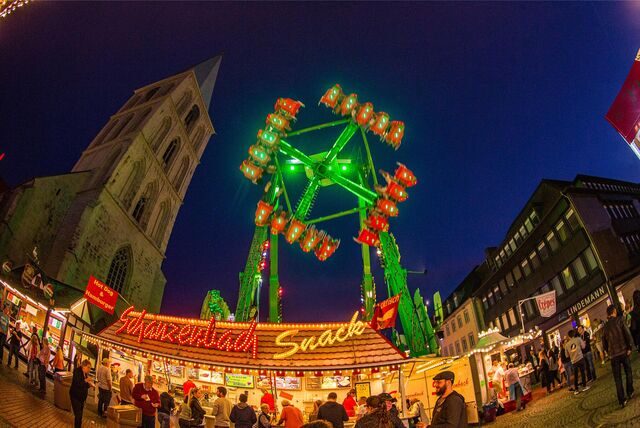 Ein Imbissstand und ein Fahrgeschäft stehen beim Stunikenmarkt in Hamm vor der Pauluskirche.