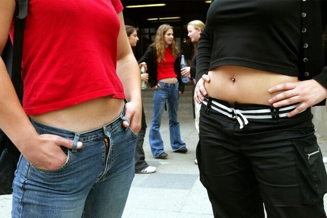 Zwei junge Frauen stehen bauchfrei auf einem Schulhof. Ihre Köpfe sind nicht zu sehen.
