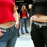 Zwei junge Frauen stehen bauchfrei auf einem Schulhof. Ihre Köpfe sind nicht zu sehen.