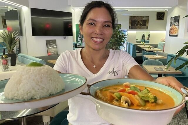 Inhaberin Thonglai hält ein Gericht in die Kamera. Es ist ein Gemüse-Curry mit Reis.