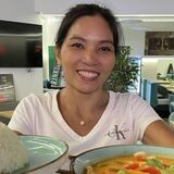 Inhaberin Thonglai hält ein Gericht in die Kamera. Es ist ein Gemüse-Curry mit Reis.