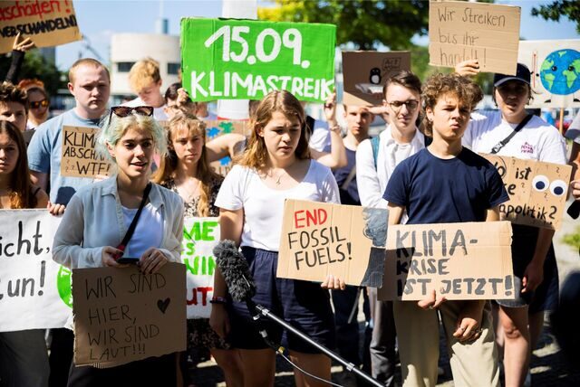 Mehrere junge Menschen halten Schilder in der Hand. Besonders auffällig in der Menge ist ein grünes Schild mit der Aufschrift „Klimastreik 15.09.“.