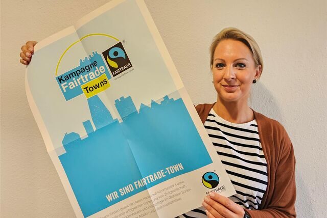 Marina Schniederjann hält ein Plakat in den Händen. Darauf das Logo der „Fairtrade Towns“.