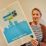 Marina Schniederjann hält ein Plakat in den Händen. Darauf das Logo der „Fairtrade Towns“.